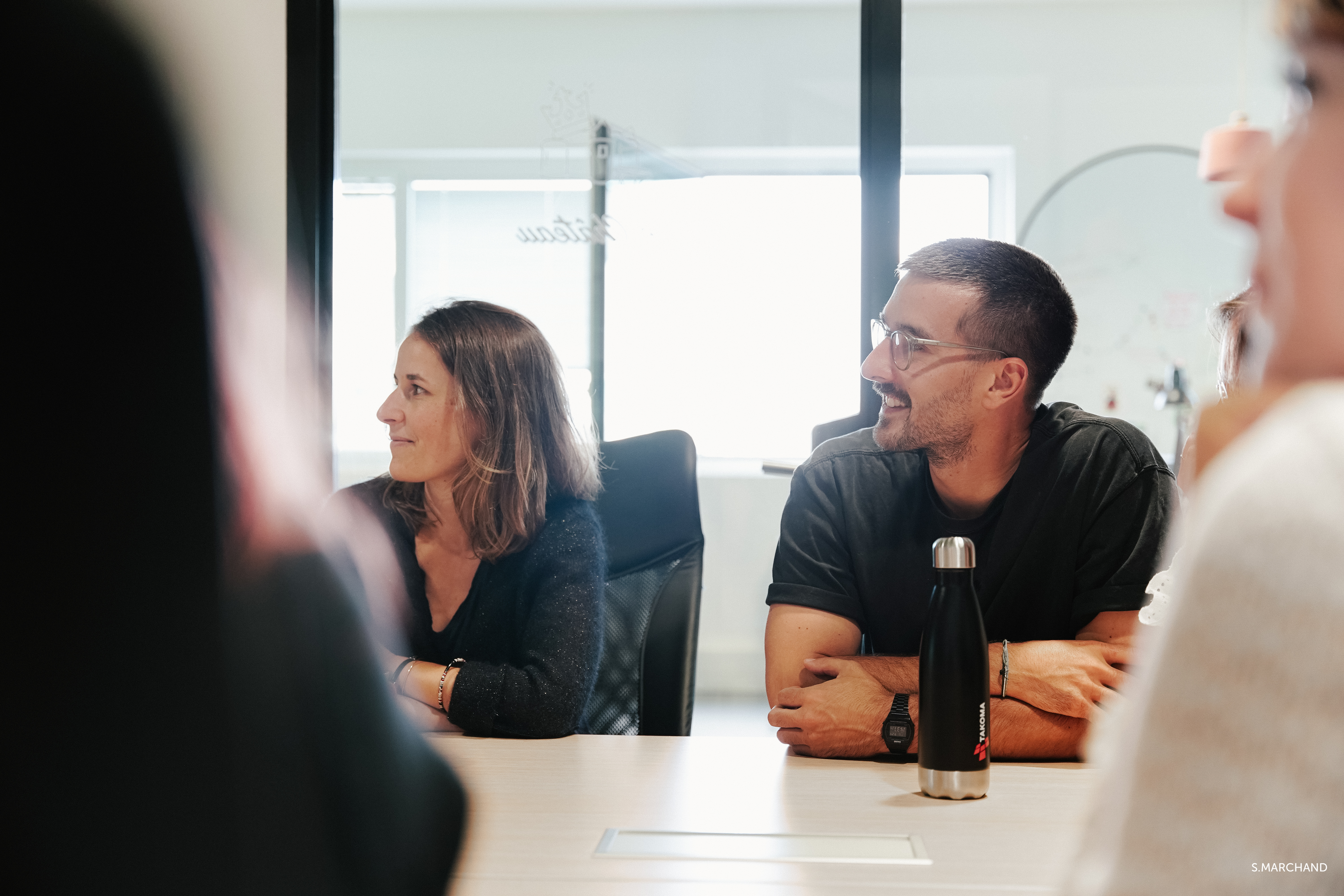 deux collaborateurs de profil regardent une présentation hors-champ.