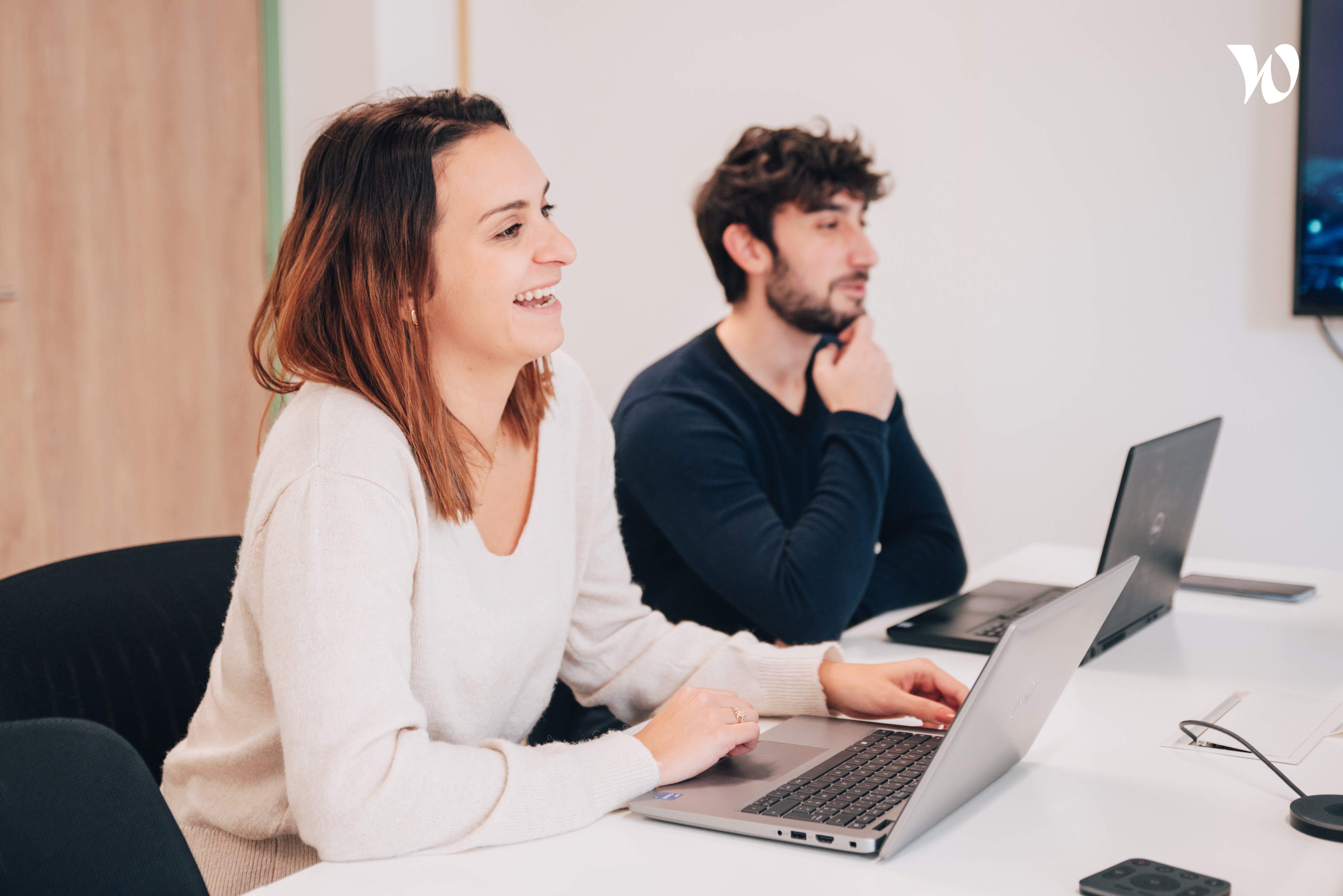 Une femme souriante devant un PC en salle de réunion