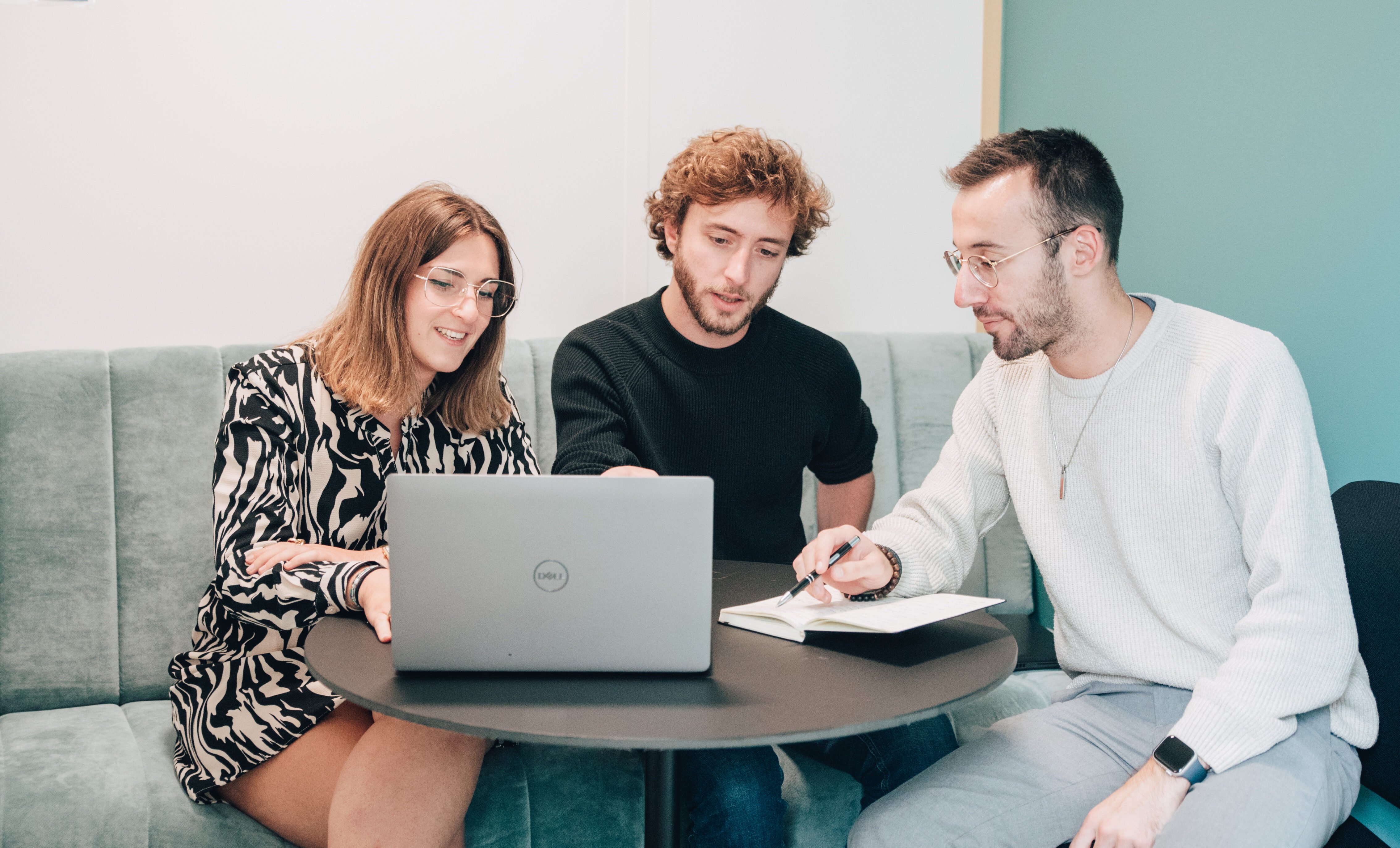 Trois collaborateurs assis à une table échangent autour d'un PC.